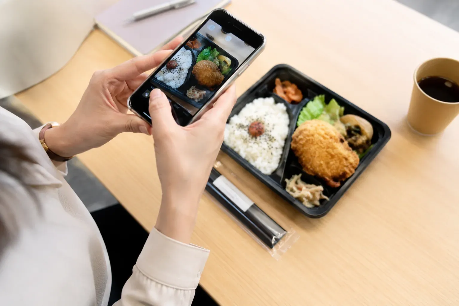 昼、机の上のお弁当をスマートフォンで撮影する女性